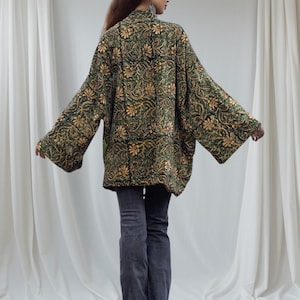 Back view of bohemian velvet kimono jacket in emerald and gold floral print, featuring wide sleeves and relaxed fit, captured on minimalist white fabric backdrop.