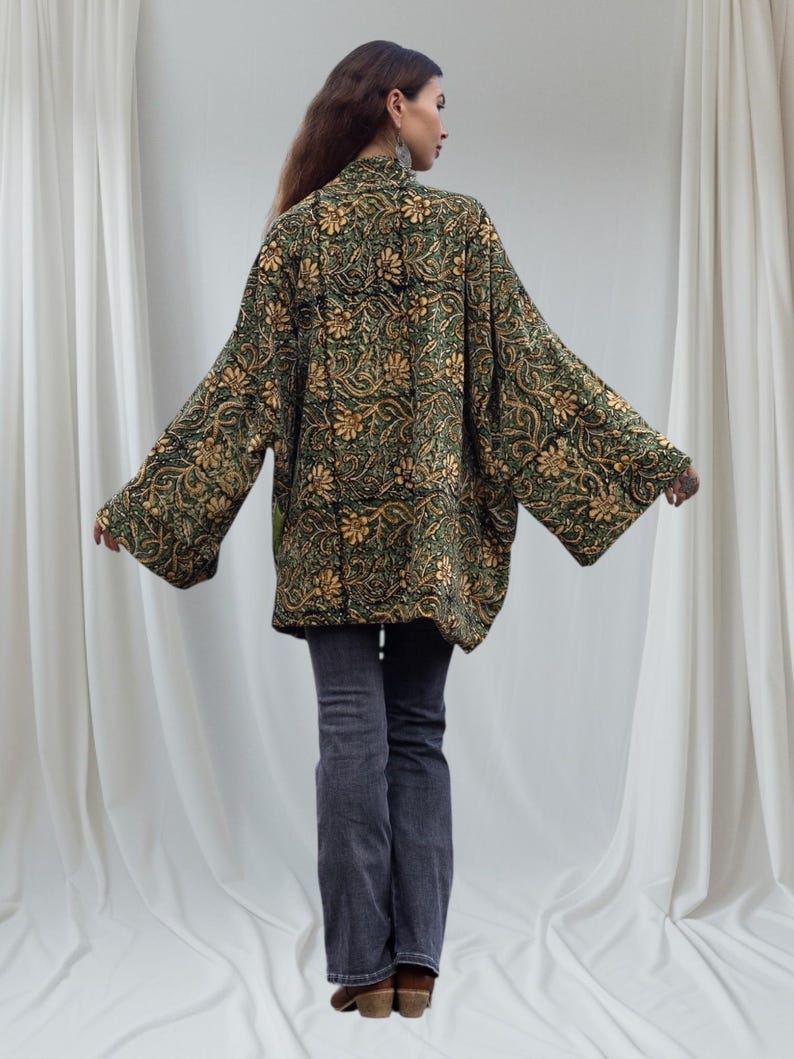 Back view of bohemian velvet kimono jacket in emerald and gold floral print, featuring wide sleeves and relaxed fit, captured on minimalist white fabric backdrop.