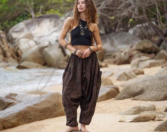 May include: A woman wearing a black halter top and brown harem pants with pockets, standing on a rock at the beach. The pants have a drawstring waist and a loose fit. She is also wearing jewelry.