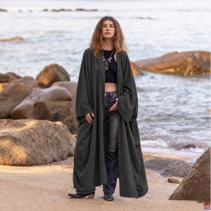 May include: A long, open-front charcoal grey duster cardigan with wide sleeves, worn over a black cropped tank top and dark grey denim jeans. The cardigan features a loose, flowing silhouette that extends to the lower calf, providing a layered look.