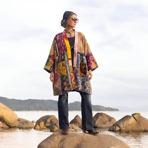 May include: A patchwork kimono-style jacket in a variety of colors and patterns, including pink, yellow, blue, and purple. The jacket is worn with dark blue jeans and a black top. The person is wearing a patterned headscarf and sunglasses.