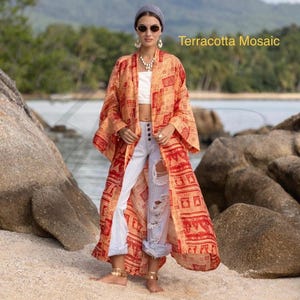 Op de afbeelding: Een lange, open kimono in oranje- en roodtinten met een mozaïekpatroon. De kimono wordt gedragen over een witte top en een lichtblauwe ripped jeans. De tekst "Terracotta Mosaic" is zichtbaar.