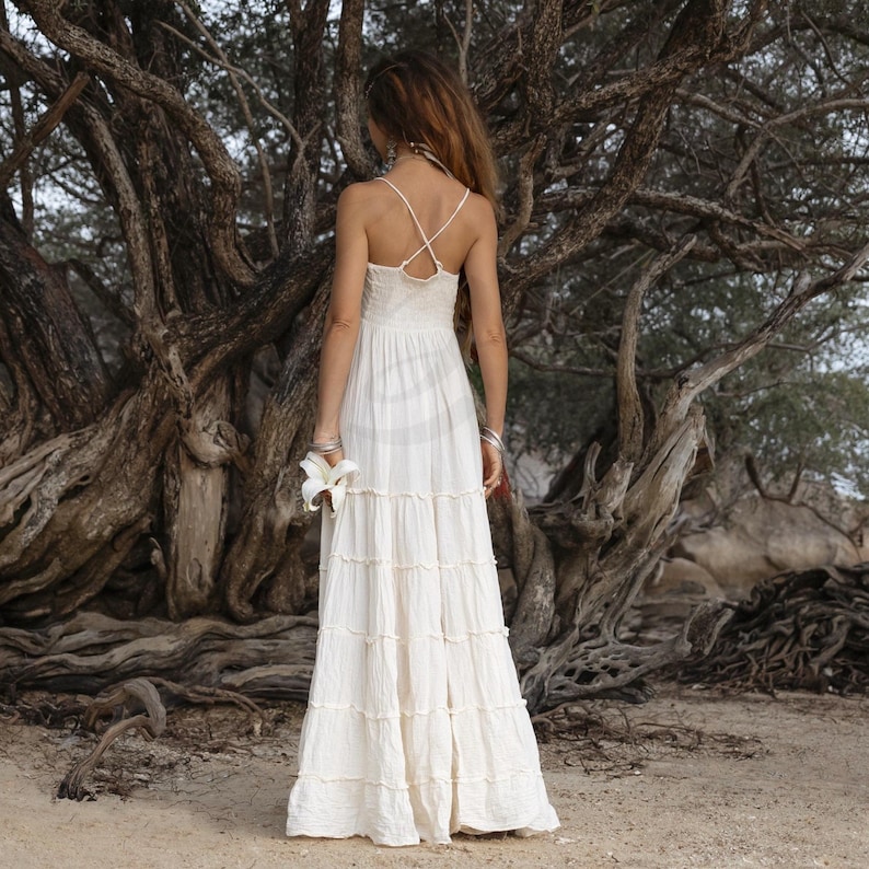 Ethical and elegant, this ZinniaPearl boho wedding dress is made from raw cotton with a plunging neckline, smocked stretch-back waist, and flowy tiered skirt. Unlined and lightweight, it’s perfect for destination weddings or outdoor elopements. Fits a wide range of sizes with comfort and beauty, including plus size brides. A soulful gown for barefoot ceremonies.
