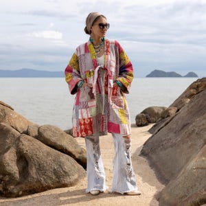 May include: A patchwork kimono-style jacket in a variety of colors, including red, yellow, and pink. The jacket has a tie closure and is worn with distressed jeans. The background features a beach and ocean.