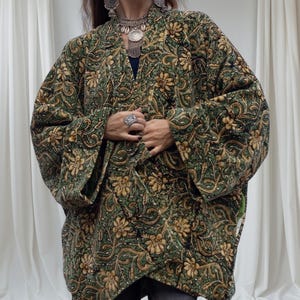 Close-up of emerald green and gold floral velvet kimono jacket showing detailed hand block print, soft texture, and artisan craftsmanship with layered silver jewelry accents.