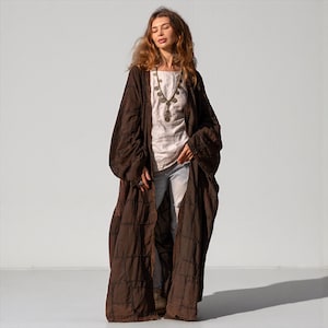 Full length studio view of the VEDA Grand Patchwork Duster in Cocoa Earth brown. The heavy cotton canvas fabric hangs with a structured, architectural drape against a clean background. This oversized kimono coat features ultra-wide sleeves and a floor-sweeping maxi length. The rich brown monochrome panels are stitched with visible raw seams, highlighting the artisan construction. A clear, detailed view of the front silhouette showing the open design and deep functional pockets.