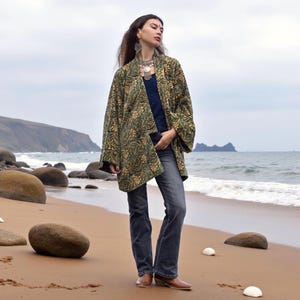 Bohemian woman wearing a handcrafted short kimono jacket in rich green and gold floral tapestry, styled with jeans and layered silver jewelry — artisan boho outfit by ZinniaPearl.