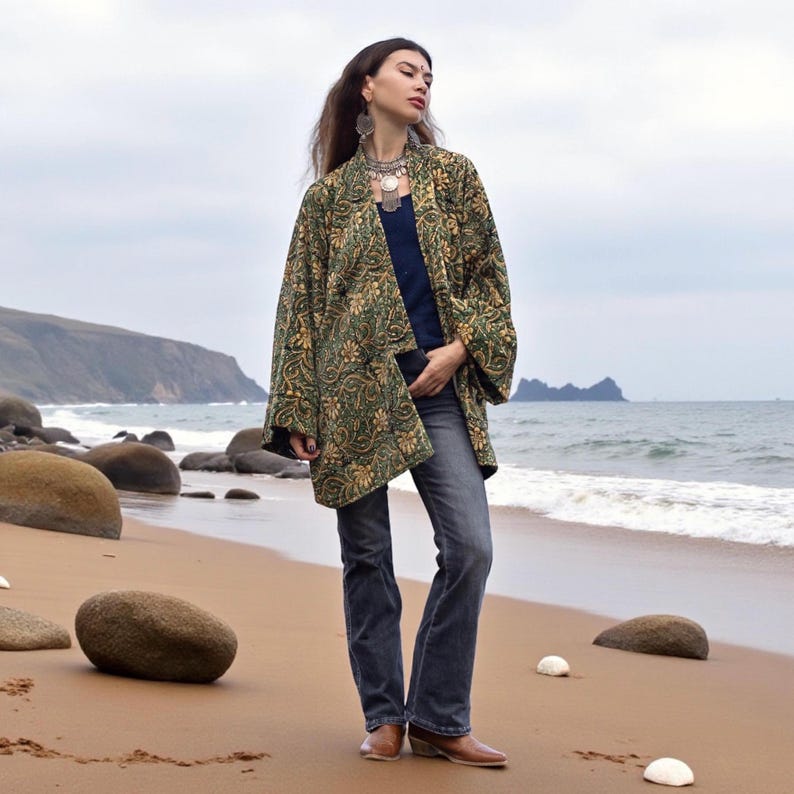 Bohemian woman wearing a handcrafted short kimono jacket in rich green and gold floral tapestry, styled with jeans and layered silver jewelry — artisan boho outfit by ZinniaPearl.