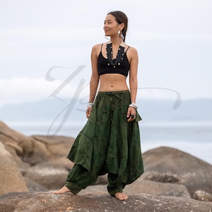 Può includere: Una persona indossa un top corto nero e pantaloni harem verde oliva su una roccia vicino al mare. I pantaloni hanno un design patchwork unico. Indossa anche gioielli.