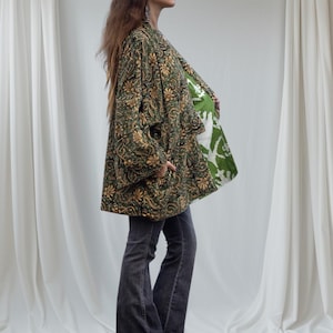 Profile view of woman in emerald floral velvet kimono jacket showing the contrasting green printed cotton lining and relaxed drape, photographed against flowing white curtains.