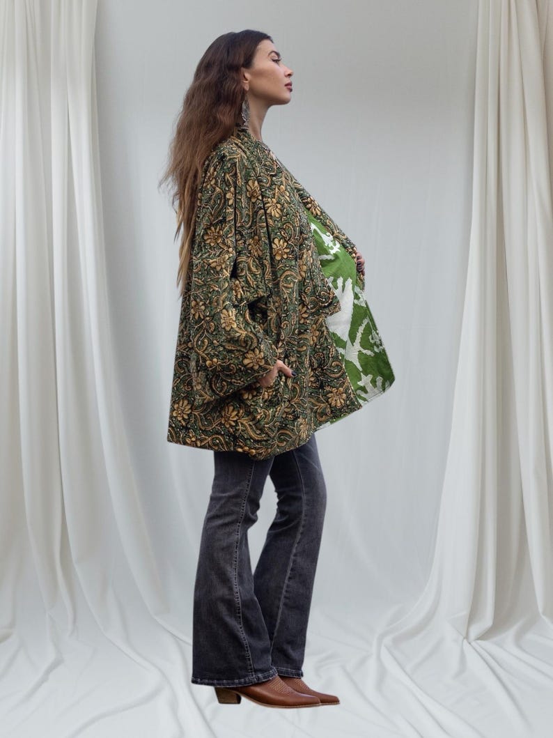 Profile view of woman in emerald floral velvet kimono jacket showing the contrasting green printed cotton lining and relaxed drape, photographed against flowing white curtains.