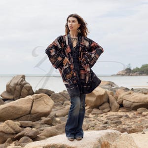 Puede incluir: Una chaqueta de manga larga abierta por delante con un diseño de patchwork en patrones rectangulares negros, marrones y tostados. La chaqueta se lleva sobre un mono de mezclilla oscuro con pantalones anchos. La prenda tiene un corte holgado.