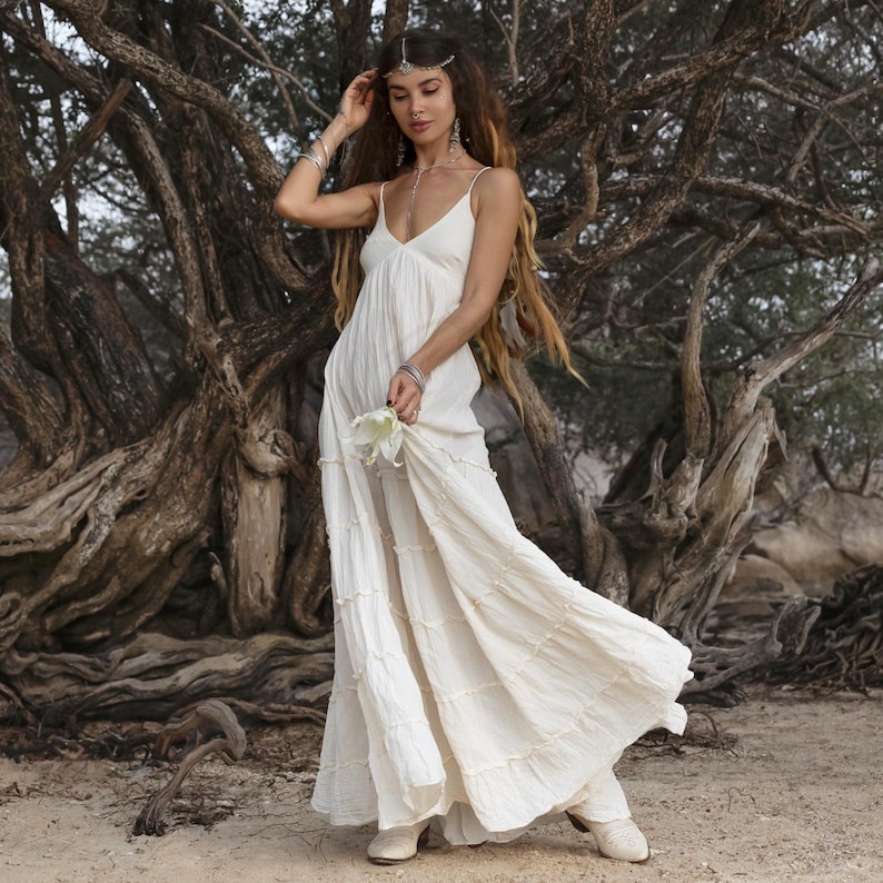ZinniaPearl’s off-white boho bridal gown in raw cotton features an airy silhouette with plunging neckline, smocked back waist, and delicate straps. Designed without lining, this dress celebrates natural texture and breathable comfort. Ideal for summer weddings, maternity shoots, or coastal elopements. Flowy and flattering for curves, in sizes up to 60” waist.