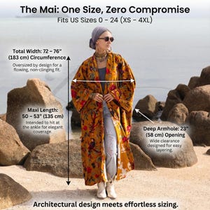 Sizing guide infographic for the "Mai" velvet kimono. Text reads: "The Mai: One Size, Zero Compromise. Fits US Sizes 0 - 24 (XS - 4XL)." Arrows indicate measurements: "Total Width: 72 – 76” (183 cm) Circumference" for a flowing fit; "Maxi Length: 50 – 53” (135 cm)" hitting at the ankle; and "Deep Armhole: 23” (58 cm) Opening" for easy layering. Caption at bottom: "Architectural design meets effortless sizing." Model is shown wearing the gold floral duster.