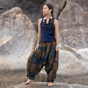 May include: A woman wearing a navy blue tank top and patchwork harem pants in shades of brown, green, and blue. The pants have a loose, comfortable fit. She is also wearing silver hoop earrings, bracelets, and a black beaded necklace.