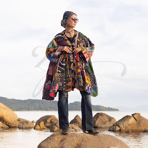 May include: A patchwork coat in a variety of colors, including black, orange, blue, and green, is worn with dark blue jeans. The coat has a unique, artistic design. The person is wearing a patterned headscarf and sunglasses.