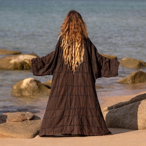 Back view of the Cocoa Earth patchwork robe. Shows the massive, grand scale of the garment. The monochrome patchwork panels are stitched together with raw, exposed seams, creating a structured, geometric look. The fabric has a crinkled, vintage finish that adds depth to the deep brown earth tone.