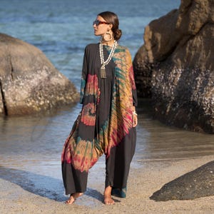 Könnte beinhalten: Dunkelgrauer Overall mit langen Ärmeln und einem Batikmuster in Rot-, Orange-, Gelb- und Grüntönen. Der Overall hat ein lockeres, fließendes Design und wird an einem Sandstrand in der Nähe des Wassers getragen.
