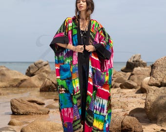 May include: A long, colorful, patchwork kimono with a black base and tie closure. The kimono has a tie-dye pattern with shades of blue, green, pink, and yellow. The model is wearing the kimono over a black top and jeans.