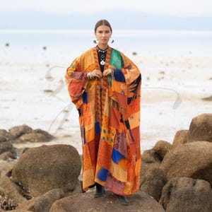 May include: A long, open-front kimono-style robe featuring a patchwork design of various fabrics in shades of orange, yellow, blue, and brown. The garment has wide sleeves and a loose, flowing silhouette, with a dark-colored top visible underneath.