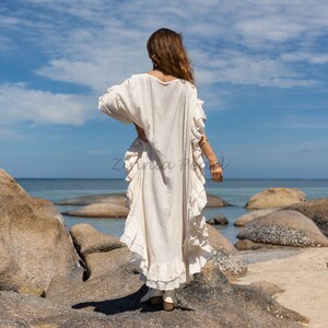 以下が含まれることがあります： フリルのある裾と袖が付いた白いマキシ丈ワンピース。ワンピースは軽量な生地で作られており、ビーチでの一日過ごすのに最適です。