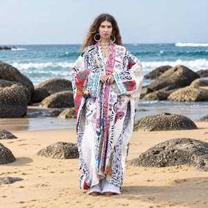 Könnte beinhalten: Ein langer, locker sitzender Kimono-Mantel mit Patchwork-Design in verschiedenen schwarzen, weißen und bunten Mustern. Das Kleidungsstück hat weite Ärmel und eine offene Vorderseite und wird über einer weißen weiten Hose mit ausgefranstem Saum getragen.