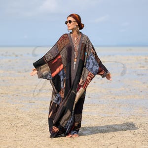 May include: A patchwork kimono-style robe in shades of brown, black, and blue. The robe features a variety of fabric patterns and textures. The person in the image is wearing sunglasses and jewelry, standing on a sandy beach.
