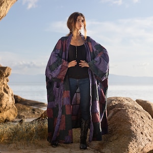 Könnte beinhalten: Ein langer, vorne offener Kimono-Mantel mit einem Patchwork-Design aus rechteckigen Stoffbahnen in den Farben Dunkelviolett, Dunkelrot und Schwarz. Das Kleidungsstück hat weite, lockere Ärmel und eine entspannte, fließende Silhouette bis unter die Knie.