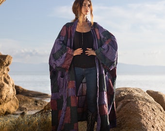 May include: A long, open-front kimono-style robe featuring a patchwork design of rectangular fabric panels in shades of deep purple, dark red, and black. The garment has wide, loose sleeves and a relaxed, flowing silhouette that reaches below the knees.