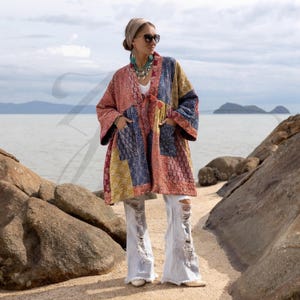 May include: A long-sleeved, open-front jacket featuring a multi-colored patchwork pattern with shades of red, blue, and yellow. The garment includes two large front pockets and is paired with light-wash, distressed denim flare jeans with frayed hems.