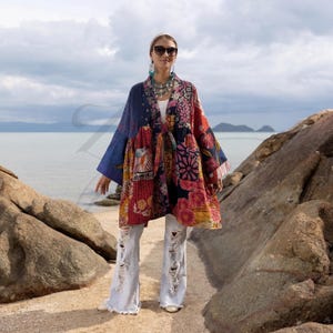 May include: A patchwork kimono-style jacket with a vibrant mix of floral and geometric patterns in red, blue, and pink. The jacket features wide sleeves and a loose fit. The model is wearing light-wash, distressed jeans.