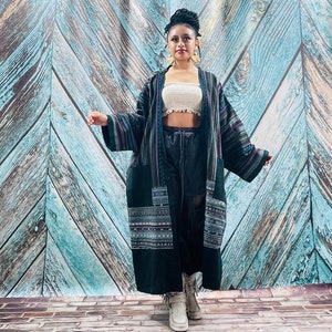 Peut inclure: Un long kimono rayé noir et violet avec des broderies complexes sur les manches et l'ourlet. Le kimono est porté sur un haut blanc court et un pantalon noir.