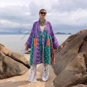 Puede incluir: Un kimono patchwork en tonos morado, turquesa y naranja. La prenda larga y abierta por delante presenta una variedad de tejidos estampados y dos bolsillos delanteros. El kimono se lleva con vaqueros claros y rotos.