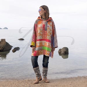 May include: A hooded tunic featuring a patchwork design with various orange, pink, yellow, and grey fabric panels. The garment has long sleeves and a loose fit. It is paired with dark blue denim jeans and grey patterned leg warmers.