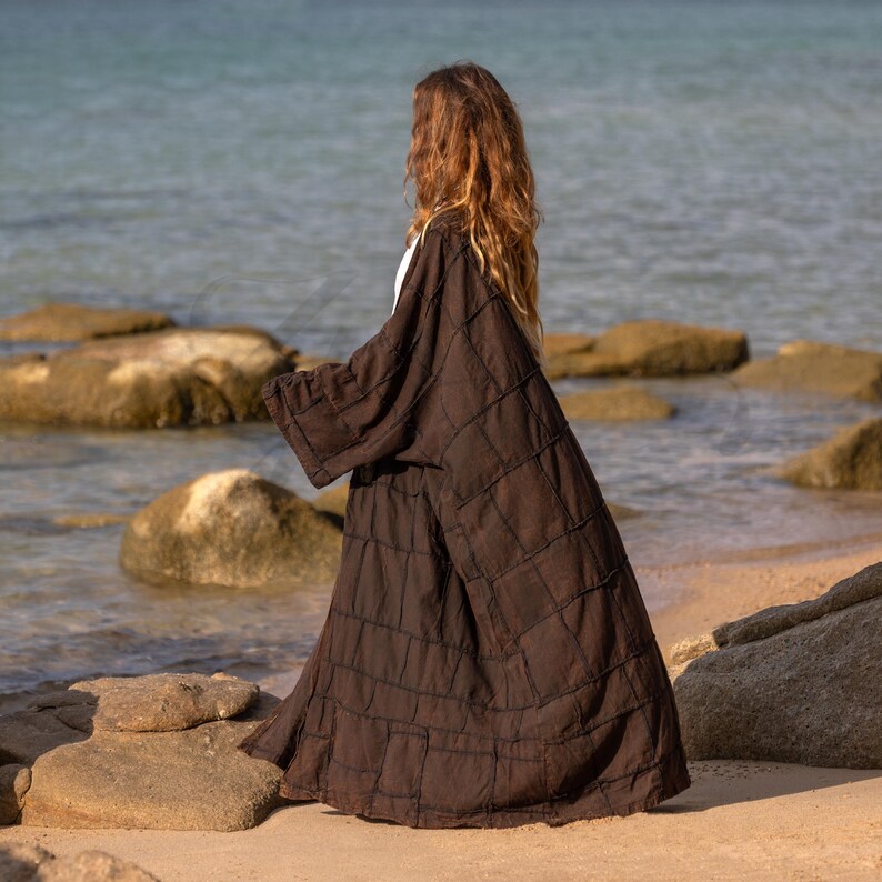 Side profile of the brown cotton canvas duster. The ultra-wide kimono sleeves drape heavily, creating an architectural silhouette. The stone-washed fabric captures the light, showing the durable workwear texture. The coat hangs loosely, perfect for Lagenlook layering over denim or dresses.