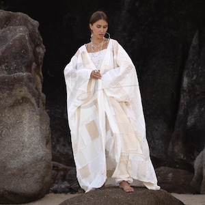 May include: A white patchwork robe with long sleeves and a matching top and pants. The robe features lace and textured fabric panels. The outfit is worn outdoors near large rocks, creating a bohemian aesthetic.
