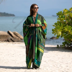 Könnte beinhalten: Ein langer Kimono mit offener Vorderseite und einem Patchwork-Design aus verschiedenen grünen, gelben und violetten Stoffmustern. Das Kleidungsstück hat weite, lockere Ärmel und eine fließende Silhouette und wird über einem schlichten, neutralen Kleid getragen.