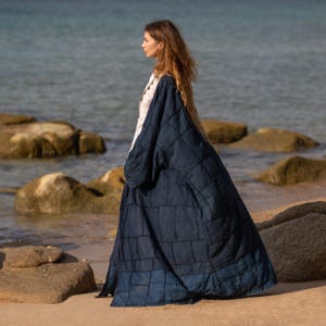 Side profile of the blue patchwork kimono. The heavy canvas fabric holds its architectural shape while allowing for movement. The midnight blue tone is rich and versatile. The raw hem details add an avant-garde, deconstructed edge to the silhouette.