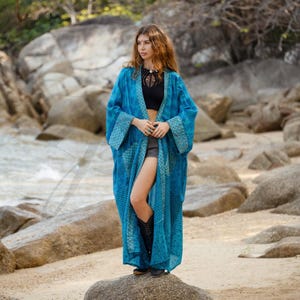 May include: A long, flowing turquoise kimono with a patterned design on the sleeves and edges. The open-front robe is worn over a black top and shorts. The kimono is made of a lightweight fabric, perfect for warm weather.