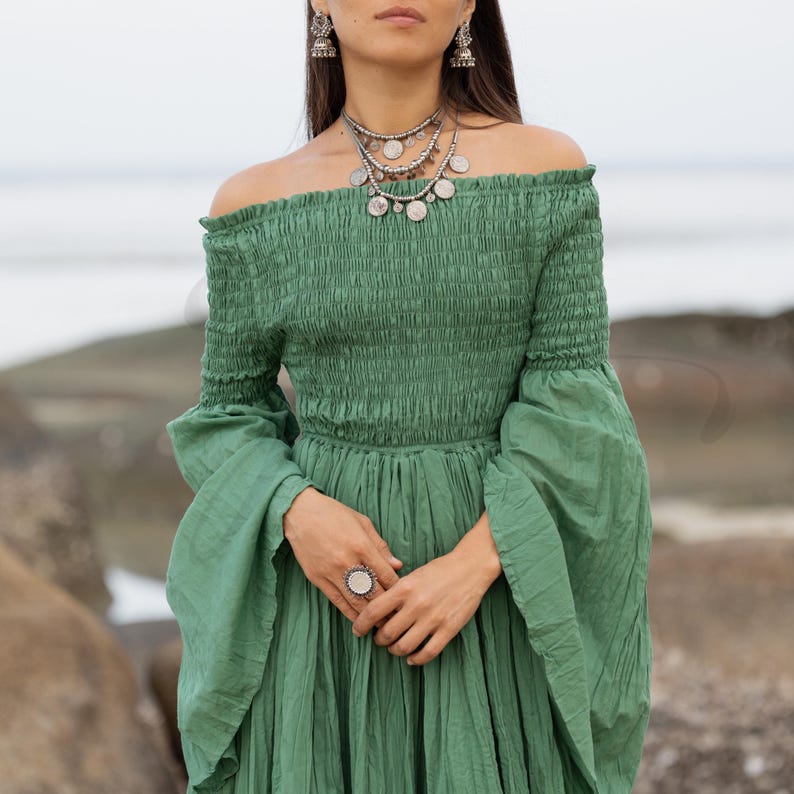 This handmade boho gown in Elderfern Green blends romantic earth tones with a tiered silhouette and elegant sleeve design. Crafted from 100% raw cotton, the Lucia dress features a stretchy off-shoulder bodice and breathable fabric that flatters all body types. Designed for barefoot brides, maternity sessions, or spiritual gatherings, it’s a timeless piece for the wild and free.