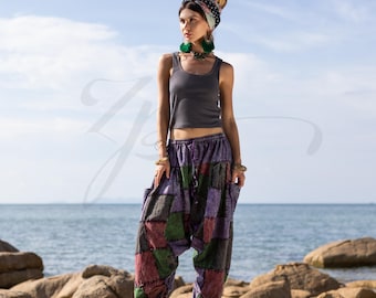 May include: A woman wearing a gray tank top and patchwork pants with a colorful pattern. She is standing on a rocky beach with the ocean in the background.