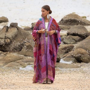 Może przedstawiać: Długie, patchworkowe kimono w odcieniach różu, fioletu i czerwieni. Ubranie z otwartym przodem ma różnorodne wzorzyste tkaniny i jest noszone na białym topie. Kimono ma długie rękawy i jest noszone na zewnątrz w pobliżu wody.