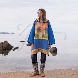 Peut inclure: Un poncho à capuche présentant un dégradé vibrant d'orange et de jaune avec un imprimé de palmiers noirs sur les panneaux avant et arrière. Le vêtement possède des manches bleu uni, une poche kangourou bleue et une patte à trois boutons.