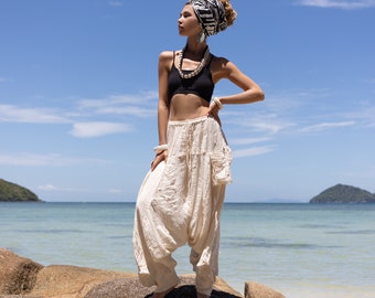 May include: Off-white, loose-fitting harem pants featuring a textured fabric, an elasticized drawstring waistband, and a square patch pocket on the left thigh. The pants have a dropped crotch design and tapered leg openings that fall to the ankles.