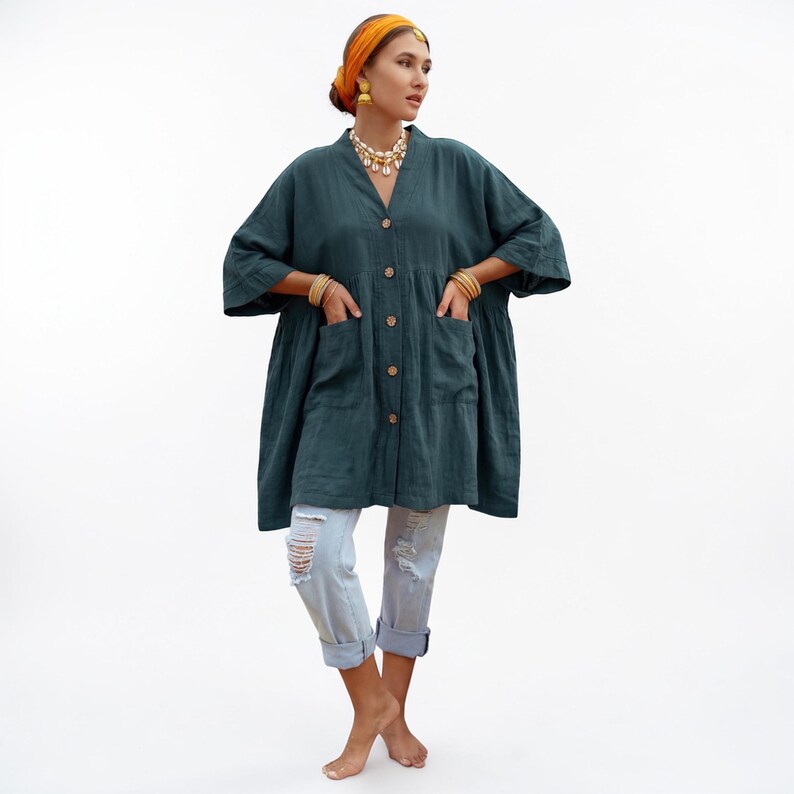 Studio-style front view of the Aria Tunic in Smoky Jade cotton gauze. The oversized boho kaftan features a button-up front with wooden buttons, wide kimono sleeves, and deep pockets. The relaxed babydoll silhouette flows away from the body for comfort and movement. Styled with cropped light denim jeans and jewelry, the breathable gauze fabric highlights effortless everyday bohemian fashion.