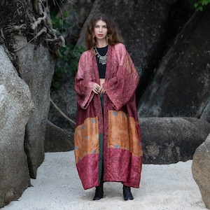 Könnte beinhalten: Ein langer, fließender Kimono in den Farbtönen Burgunder, Rosa und Orange. Der Kimono hat ein Patchwork-Design mit rechteckigen Stoffbahnen mit Muster. Die Ärmel sind weit und das Kleidungsstück scheint aus einem leichten Material zu sein.
