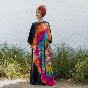 May include: A long, flowing tie-dye dress with a button-up front. The dress is a mix of black, orange, pink, blue, and yellow. The model is wearing a red turban.
