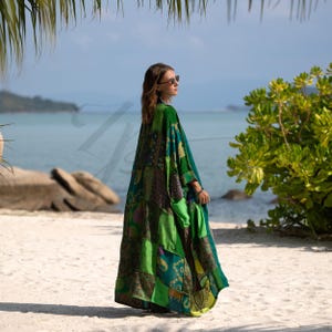 Side view of the Harper Jade Emerald Oasis Kimono, crafted from upcycled vintage silk saris in vibrant greens and blues with intricate patchwork motifs. The bohemian robe flows gracefully in the ocean breeze, showing its lightweight silk fabric and relaxed drape. Designed as a one-of-a-kind kimono duster for festivals, resort wear, and everyday boho layering.