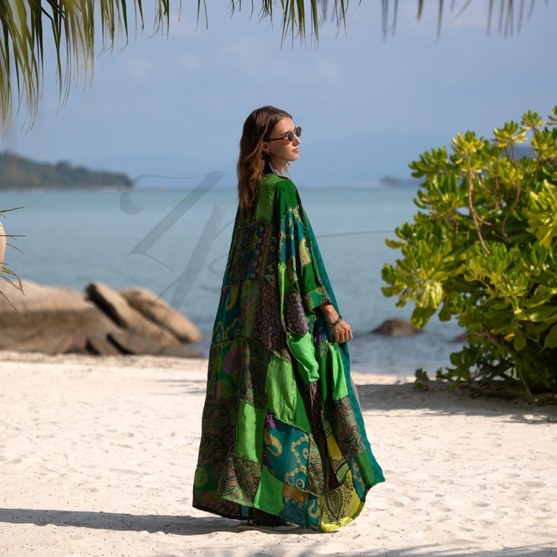 Side view of the Harper Jade Emerald Oasis Kimono, crafted from upcycled vintage silk saris in vibrant greens and blues with intricate patchwork motifs. The bohemian robe flows gracefully in the ocean breeze, showing its lightweight silk fabric and relaxed drape. Designed as a one-of-a-kind kimono duster for festivals, resort wear, and everyday boho layering.