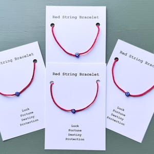 May include: Four red string bracelets with a blue evil eye charm are displayed on white cards. The cards are labeled "Red String Bracelet" and include the words "Luck, Fortune, Destiny, Protection."
